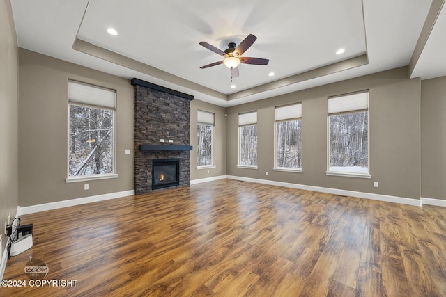 unfurnished living room with wood-type flooring, a raised ceiling, ceiling fan, and a stone fireplace