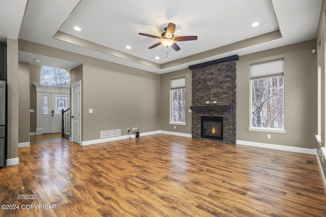 unfurnished living room with plenty of natural light, a stone fireplace, a raised ceiling, and dark wood-type flooring