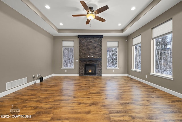 unfurnished living room with ceiling fan, a fireplace, a tray ceiling, and dark wood-type flooring