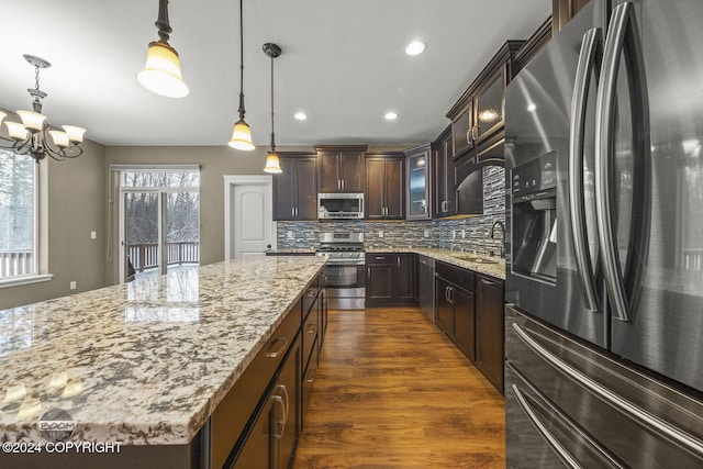 kitchen featuring a center island, decorative light fixtures, decorative backsplash, dark brown cabinets, and appliances with stainless steel finishes