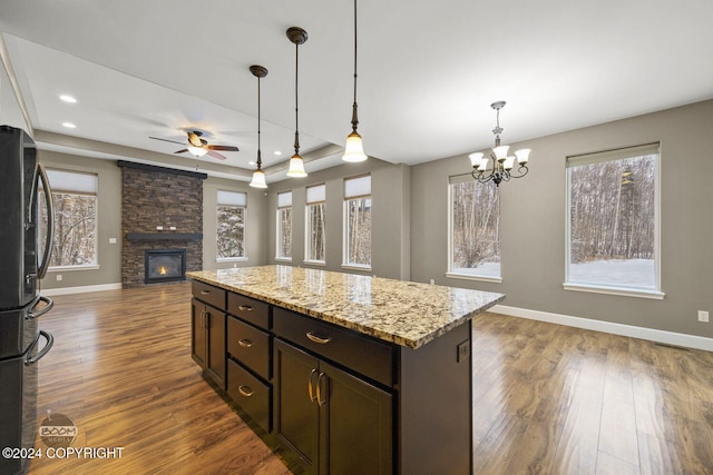 kitchen with ceiling fan with notable chandelier, a fireplace, decorative light fixtures, light stone counters, and stainless steel refrigerator