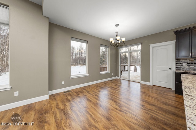 unfurnished dining area with dark wood-type flooring and an inviting chandelier