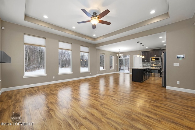 unfurnished living room with ceiling fan with notable chandelier, dark hardwood / wood-style floors, and a raised ceiling