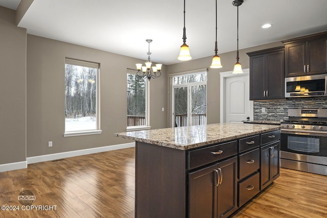 kitchen featuring decorative backsplash, appliances with stainless steel finishes, dark brown cabinetry, a kitchen island, and hanging light fixtures