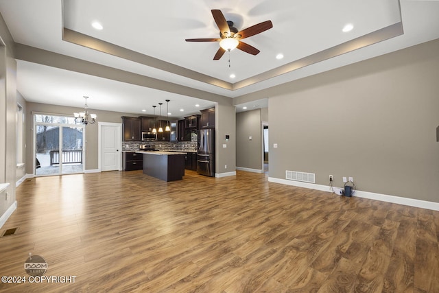 unfurnished living room with dark hardwood / wood-style flooring, ceiling fan with notable chandelier, and a tray ceiling