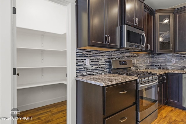 kitchen with dark brown cabinets, dark hardwood / wood-style flooring, light stone counters, and stainless steel appliances