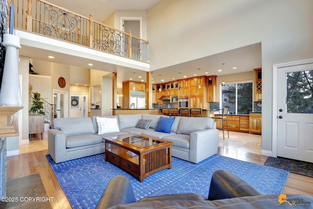 living room with a towering ceiling, light wood finished floors, baseboards, and recessed lighting