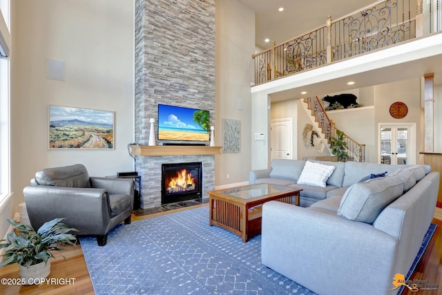 living area with french doors, a fireplace, stairway, a towering ceiling, and wood finished floors