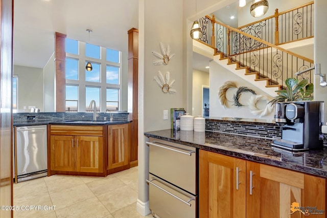 kitchen featuring tasteful backsplash, brown cabinetry, dark stone counters, stainless steel dishwasher, and a sink