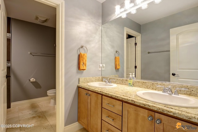 bathroom with double vanity, a sink, toilet, and baseboards