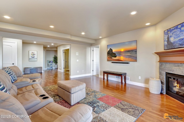 living room featuring a stone fireplace, recessed lighting, wood finished floors, and baseboards