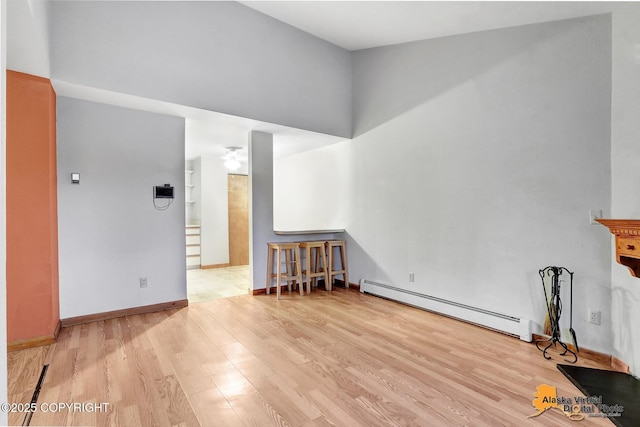 living room with a towering ceiling, a baseboard heating unit, and light hardwood / wood-style flooring