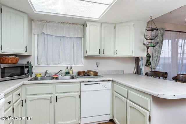 kitchen with a skylight, dishwasher, sink, kitchen peninsula, and white cabinets