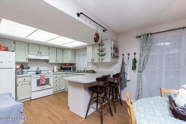 kitchen with kitchen peninsula, a breakfast bar, a textured ceiling, white appliances, and light hardwood / wood-style flooring