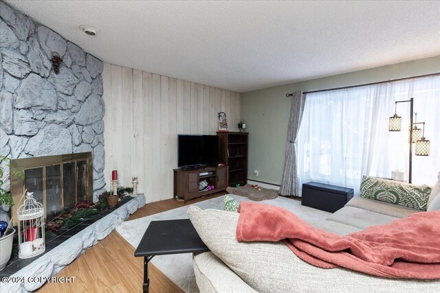 living room featuring baseboard heating, wood walls, a textured ceiling, a fireplace, and hardwood / wood-style flooring