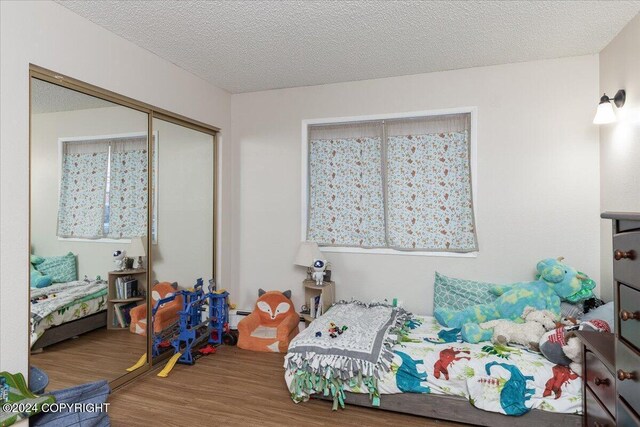 bedroom with hardwood / wood-style floors, a textured ceiling, baseboard heating, and a closet