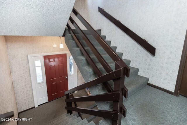 stairway with carpet flooring, a textured ceiling, and vaulted ceiling