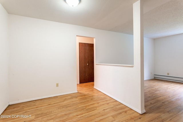 empty room featuring a textured ceiling, light hardwood / wood-style flooring, and baseboard heating