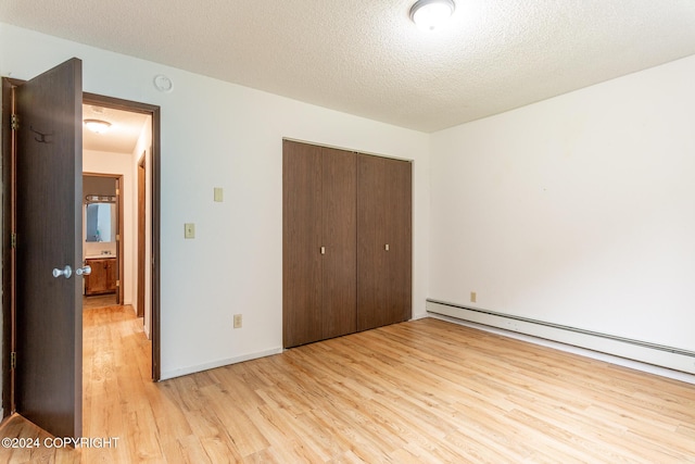 unfurnished bedroom with a textured ceiling, light hardwood / wood-style floors, baseboard heating, and a closet