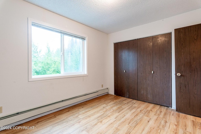 unfurnished bedroom featuring a textured ceiling, a closet, baseboard heating, and light hardwood / wood-style flooring