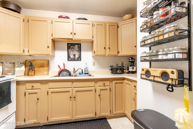 kitchen with light brown cabinetry, sink, and white range