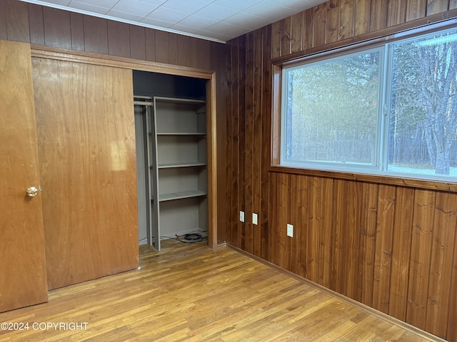 unfurnished bedroom with light hardwood / wood-style floors, wooden walls, and a closet