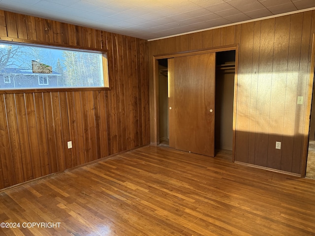 unfurnished bedroom featuring hardwood / wood-style floors, a closet, and wooden walls