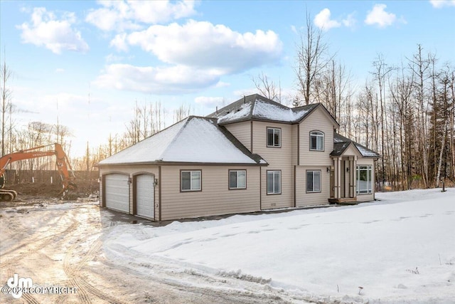 snow covered back of property featuring a garage