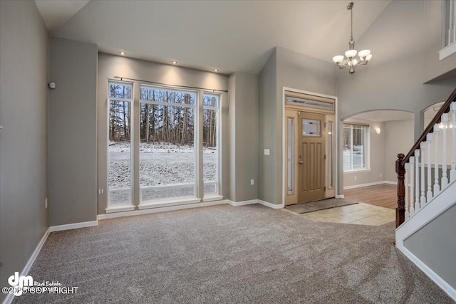 entrance foyer featuring high vaulted ceiling, light colored carpet, and an inviting chandelier