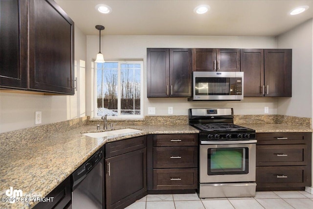 kitchen featuring sink, appliances with stainless steel finishes, hanging light fixtures, light stone counters, and dark brown cabinetry