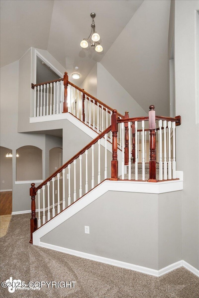 stairs featuring carpet floors, an inviting chandelier, and high vaulted ceiling