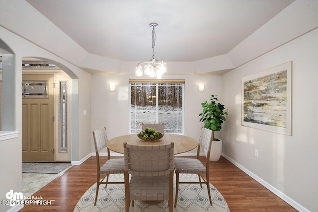 dining room with an inviting chandelier, a tray ceiling, and wood-type flooring