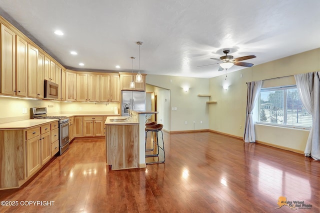 kitchen with a breakfast bar, light brown cabinetry, decorative light fixtures, an island with sink, and stainless steel appliances