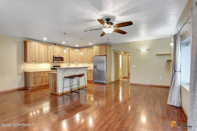 kitchen with a kitchen island, decorative light fixtures, a kitchen bar, stainless steel appliances, and light brown cabinets