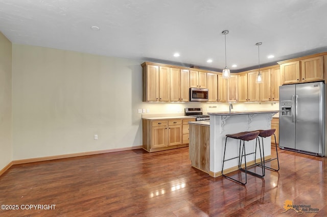 kitchen with pendant lighting, appliances with stainless steel finishes, a kitchen breakfast bar, a center island, and light brown cabinetry