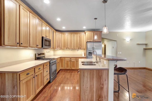 kitchen featuring appliances with stainless steel finishes, a breakfast bar area, hanging light fixtures, a kitchen island with sink, and light hardwood / wood-style floors