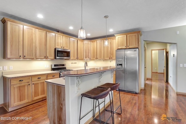 kitchen featuring a breakfast bar area, dark wood-type flooring, stainless steel appliances, a center island with sink, and decorative light fixtures