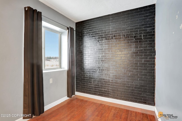 empty room with wood-type flooring and brick wall