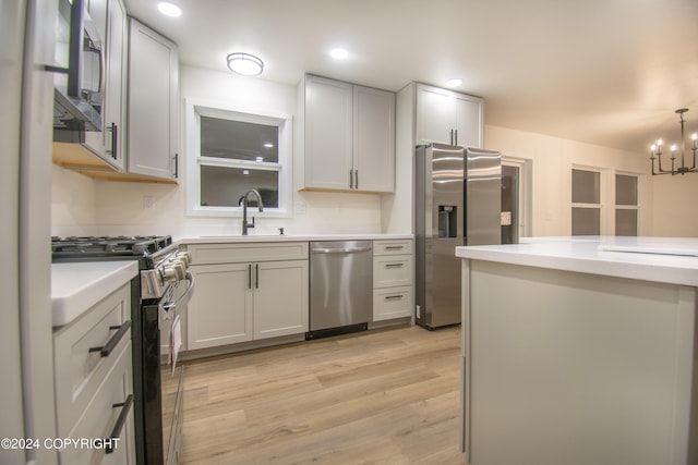 kitchen with appliances with stainless steel finishes, light wood-type flooring, sink, decorative light fixtures, and a chandelier