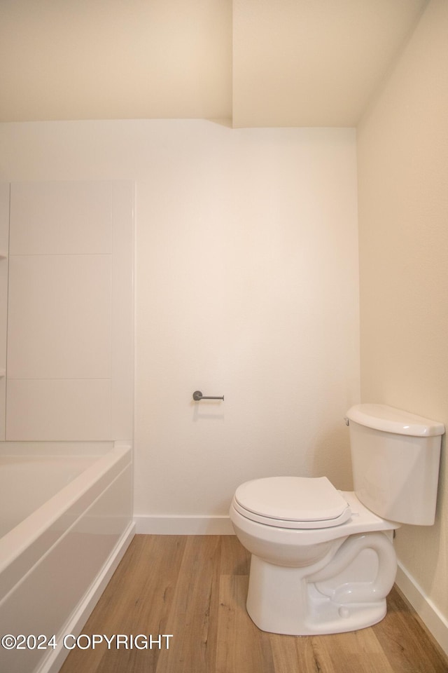 bathroom with a washtub, hardwood / wood-style flooring, and toilet