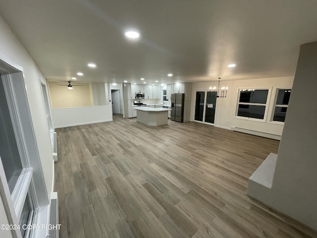 unfurnished living room featuring hardwood / wood-style floors, ceiling fan with notable chandelier, and a baseboard radiator