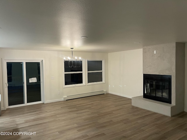 unfurnished living room with a premium fireplace, a notable chandelier, a baseboard heating unit, hardwood / wood-style floors, and a textured ceiling