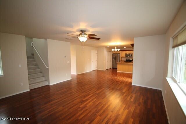 unfurnished living room featuring dark hardwood / wood-style floors and ceiling fan with notable chandelier