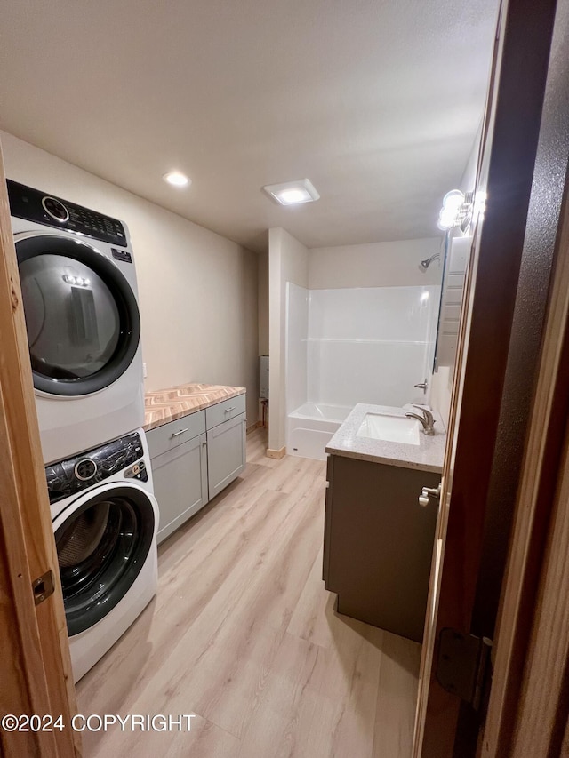 laundry room with sink, light wood-type flooring, and stacked washer / dryer