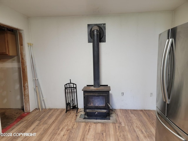 room details featuring stainless steel refrigerator, light hardwood / wood-style flooring, and a wood stove