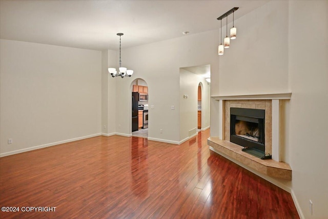 unfurnished living room featuring hardwood / wood-style floors, a notable chandelier, and a tiled fireplace