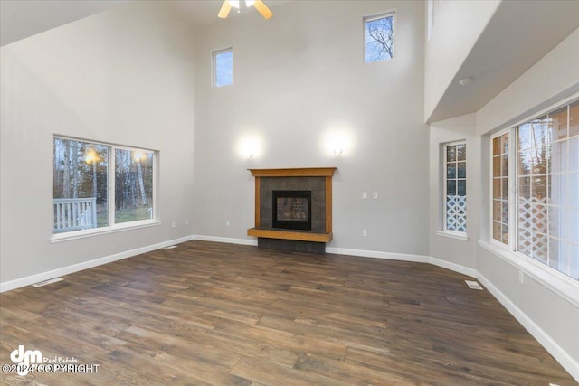 unfurnished living room featuring ceiling fan, a towering ceiling, dark hardwood / wood-style floors, and a tiled fireplace