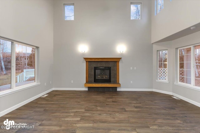 unfurnished living room featuring a high ceiling, a tile fireplace, dark hardwood / wood-style floors, and a wealth of natural light