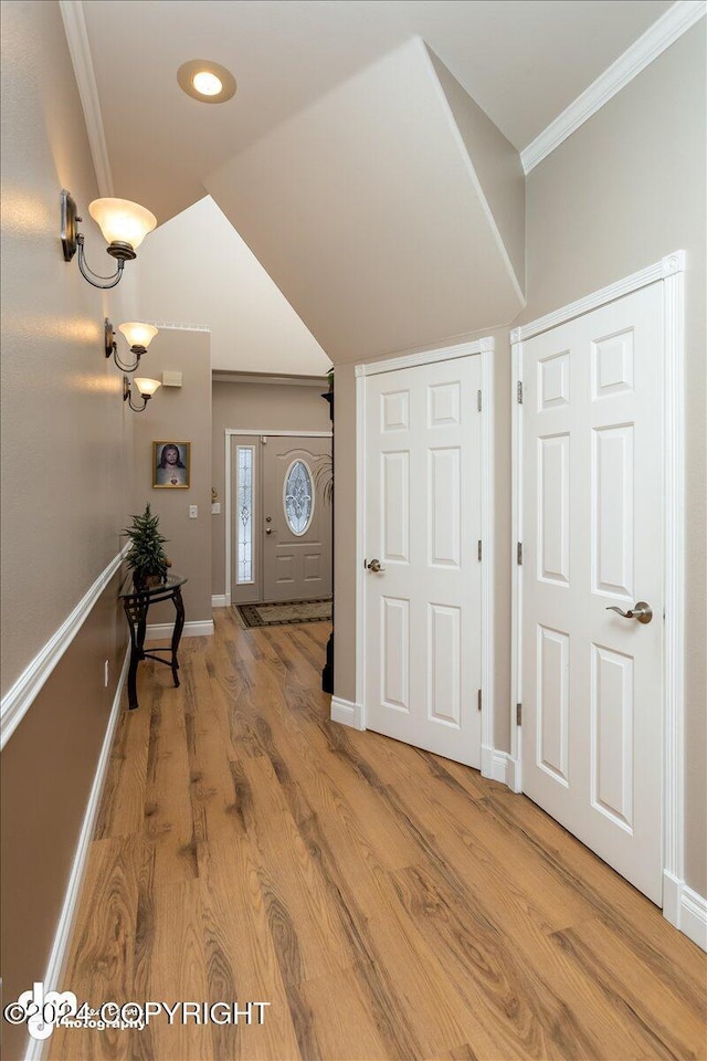 foyer entrance featuring hardwood / wood-style flooring, crown molding, and vaulted ceiling