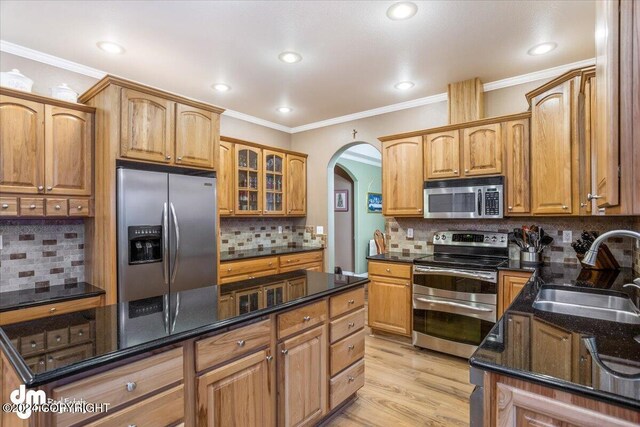 kitchen featuring sink, crown molding, dark stone countertops, appliances with stainless steel finishes, and light hardwood / wood-style floors